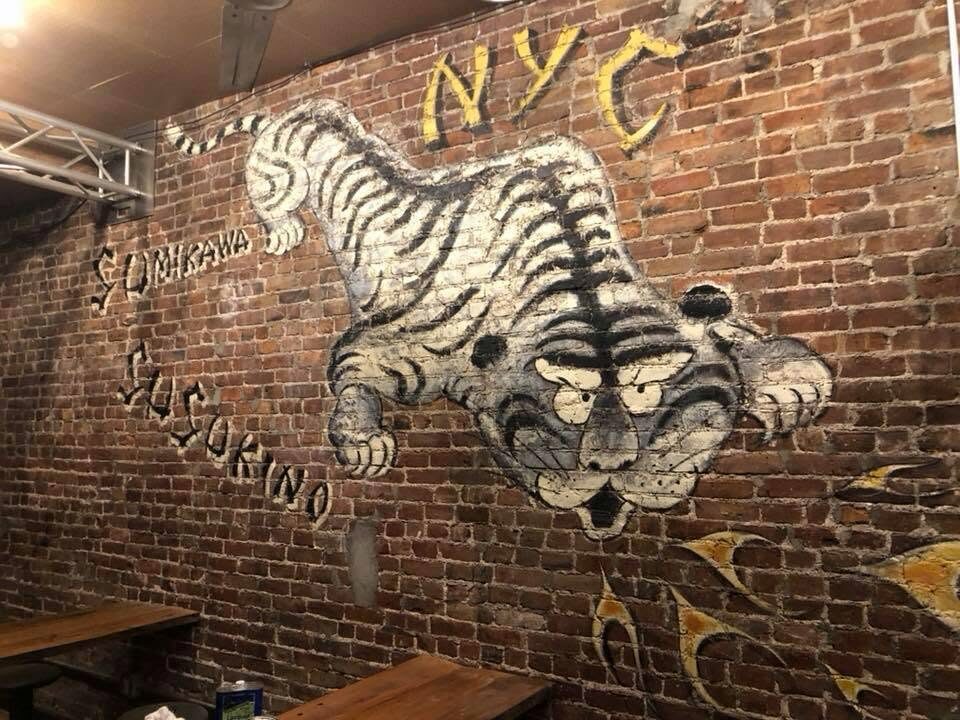 Hand-painted white tiger mural on exposed brick in the Menkoi Sao dining room